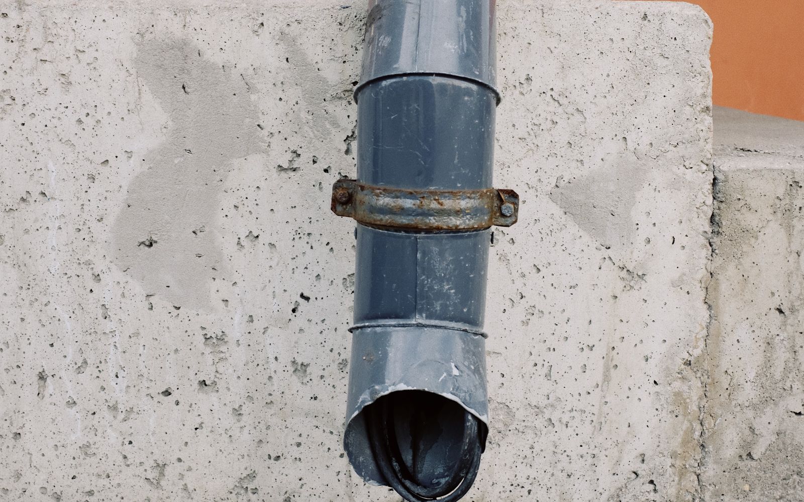 Metal rainwater downspout attached to a concrete exterior wall
