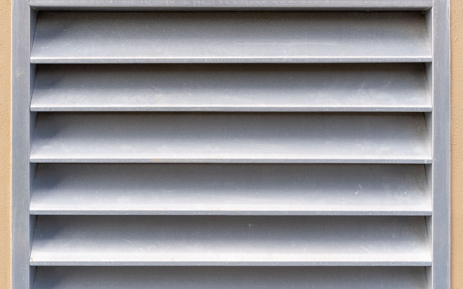 Close-up of a rectangular metal ventilation grille on an exterior wall
